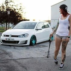a woman walking with a tennis racquet next to a white vw golf