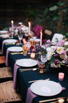 a long table is set with purple and white flowers, candles, and place settings