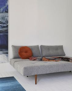 a gray couch sitting on top of a white floor next to a wall mounted painting