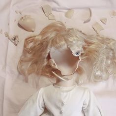 a doll with blonde hair laying on top of a white sheet