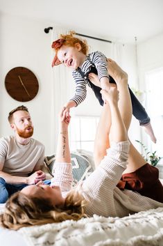 a man and woman sitting on top of a bed while holding a child up in the air