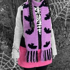 a woman wearing a purple and black scarf with bats on it, standing in front of a tree