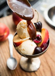 an ice cream sundae with chocolate sauce and fruit in it on a wooden table