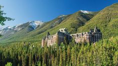 a large building sitting on top of a lush green hillside next to trees and mountains