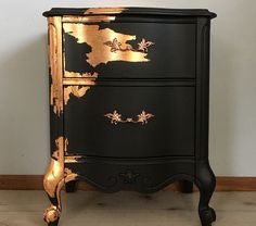 a black and gold painted chest of drawers on the floor next to a white wall