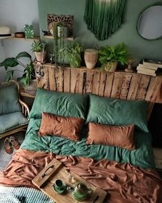 a bed covered in green and brown pillows next to a wooden headboard with potted plants on it