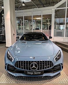 the front end of a blue mercedes sls parked in a showroom with its hood up