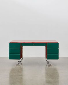 a green and red desk sitting on top of a cement floor next to a white wall