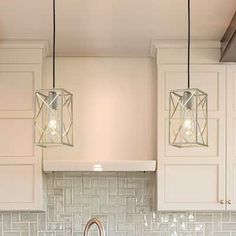 three lights hanging from the ceiling above a sink in a kitchen with white cabinets and marble counter tops