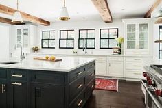 a large kitchen with white cabinets and black counter tops, along with wooden beams in the ceiling