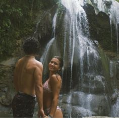 a man and woman standing in front of a waterfall with water cascading over them