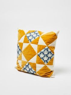 a yellow and blue pillow with white flowers on it's side, sitting on a white surface