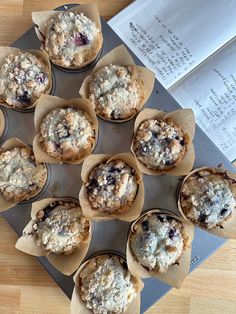 twelve muffins with blueberries in them on a tray next to an open book