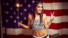 a beautiful young woman standing in front of an american flag holding a lit sparkler