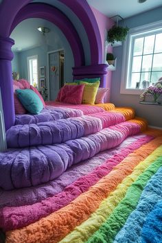 a rainbow colored bed with pillows and blankets on it in a room that looks like an arch