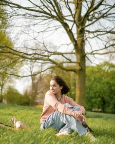 a woman is sitting in the grass with her dog and looking at something behind her