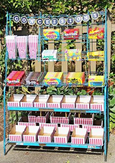 an outdoor carnival stand with boxes and cups on it's sides, in front of some bushes