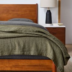 a bed with a green bedspread sitting on top of it next to a night stand