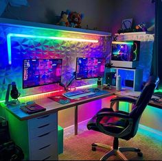 a computer desk with two monitors and a keyboard on it in a room lit up by colorful lights