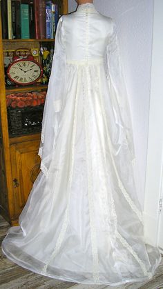 a white wedding gown on display in front of a bookshelf with a clock