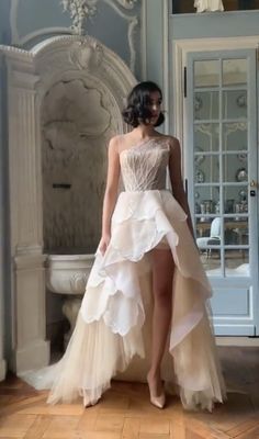 a woman in a white dress standing on a wooden floor next to a wall and door