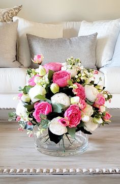 a vase filled with pink and white flowers on top of a wooden table next to a couch