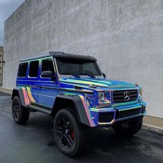 a blue mercedes g - class parked in front of a building with graffiti on it