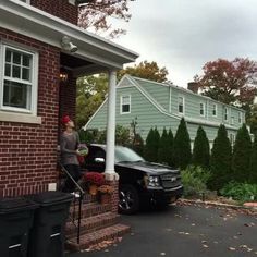 a woman standing on the front porch of a house next to a black pickup truck