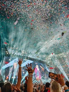 many people are holding their hands up in the air as confetti falls from above them