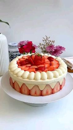 a cake with strawberries on top is sitting on a plate next to some flowers