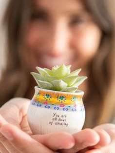 a woman holding a small ceramic pot with a succulent in it's hand