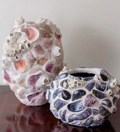 two vases sitting on top of a wooden table next to each other with shells in them
