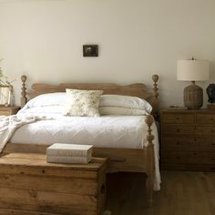 a bed sitting in a bedroom next to a dresser and lamp on top of a hard wood floor