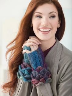 a woman with long red hair wearing a gray coat and matching gloves smiles at the camera