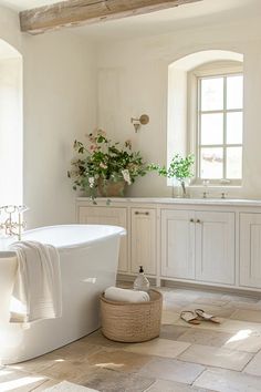 a white bath tub sitting in a bathroom next to a sink and window with potted plants