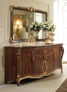 a large mirror sitting on top of a wooden cabinet next to a vase filled with flowers