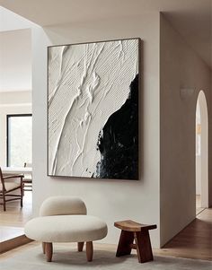 an abstract painting hangs on the wall next to a white chair and footstool