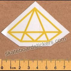 a white and yellow diamond sticker on a brown background next to a measuring ruler