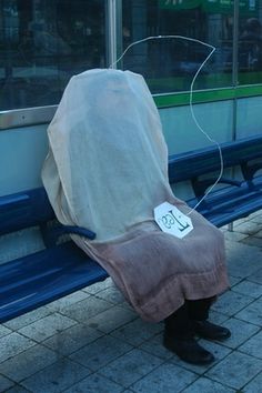 a person sitting on a bench with a cover over their head and earphones attached to it