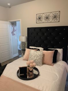 a black headboard on a white bed with pink pillows and decorative artwork above it