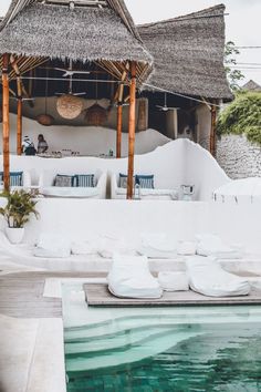 an outdoor pool with lounge chairs and thatched roof