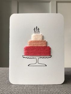 a card with a cake on it and two candles in the middle, sitting on top of a table