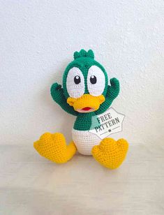 a crocheted green bird holding a free pattern for this stuffed animal is sitting in front of a white wall