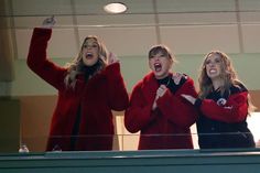 two women in red jackets and one woman with her hands up while standing on a balcony