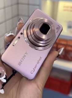 a woman holding up a pink camera in her hand with white flowers on the side