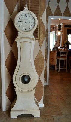 a white clock sitting in the middle of a living room next to a dining room