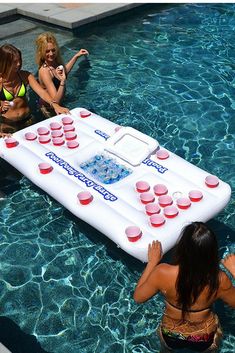 three women are in the pool playing with an inflatable board game while another woman watches