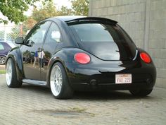 the back end of a black car parked on a brick road next to a building