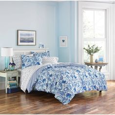 a blue and white bed in a bedroom next to a table with a lamp on it