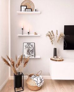 a living room with white walls and shelves filled with vases, plants and pictures